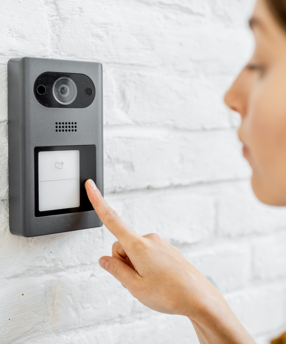 Woman pressing a video cctv doorbell on a white brick wall