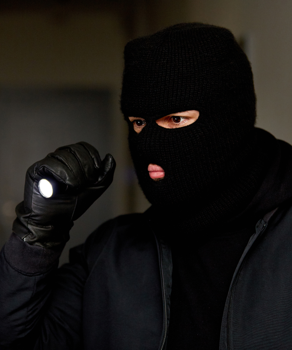 Burglar wearing a black balaclava and gloves holding a flashlight in a dark room