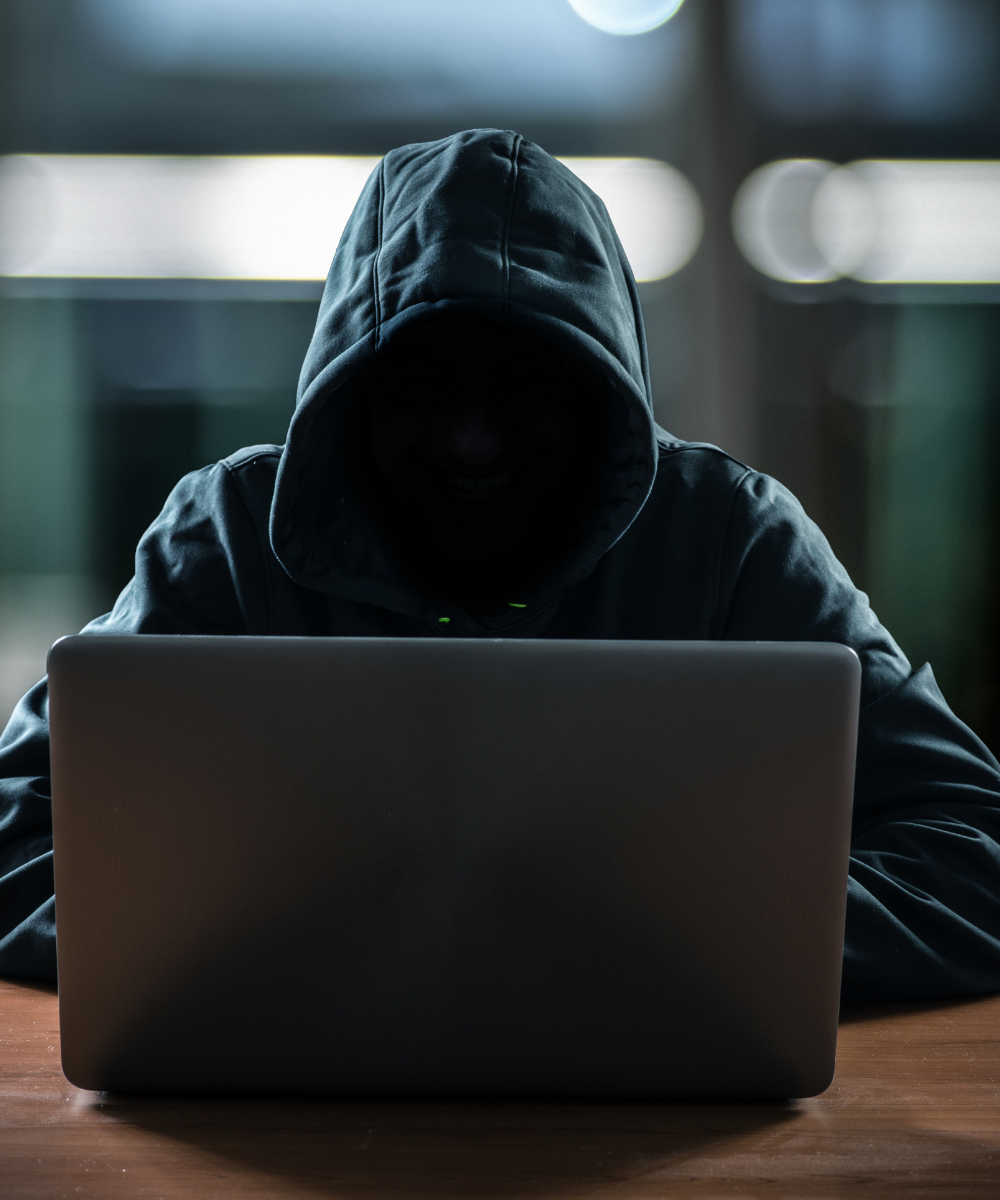 Hacker wearing a hooded jacket using a laptop in a dimly lit room