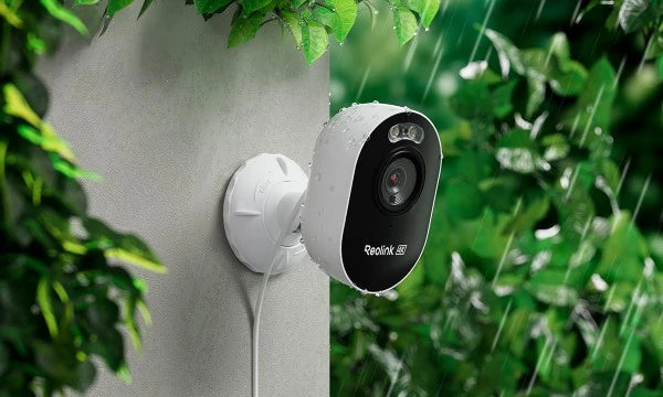 Reolink Lumus Pro Outdoor security camera mounted on a wall with greenery in the background in the rain