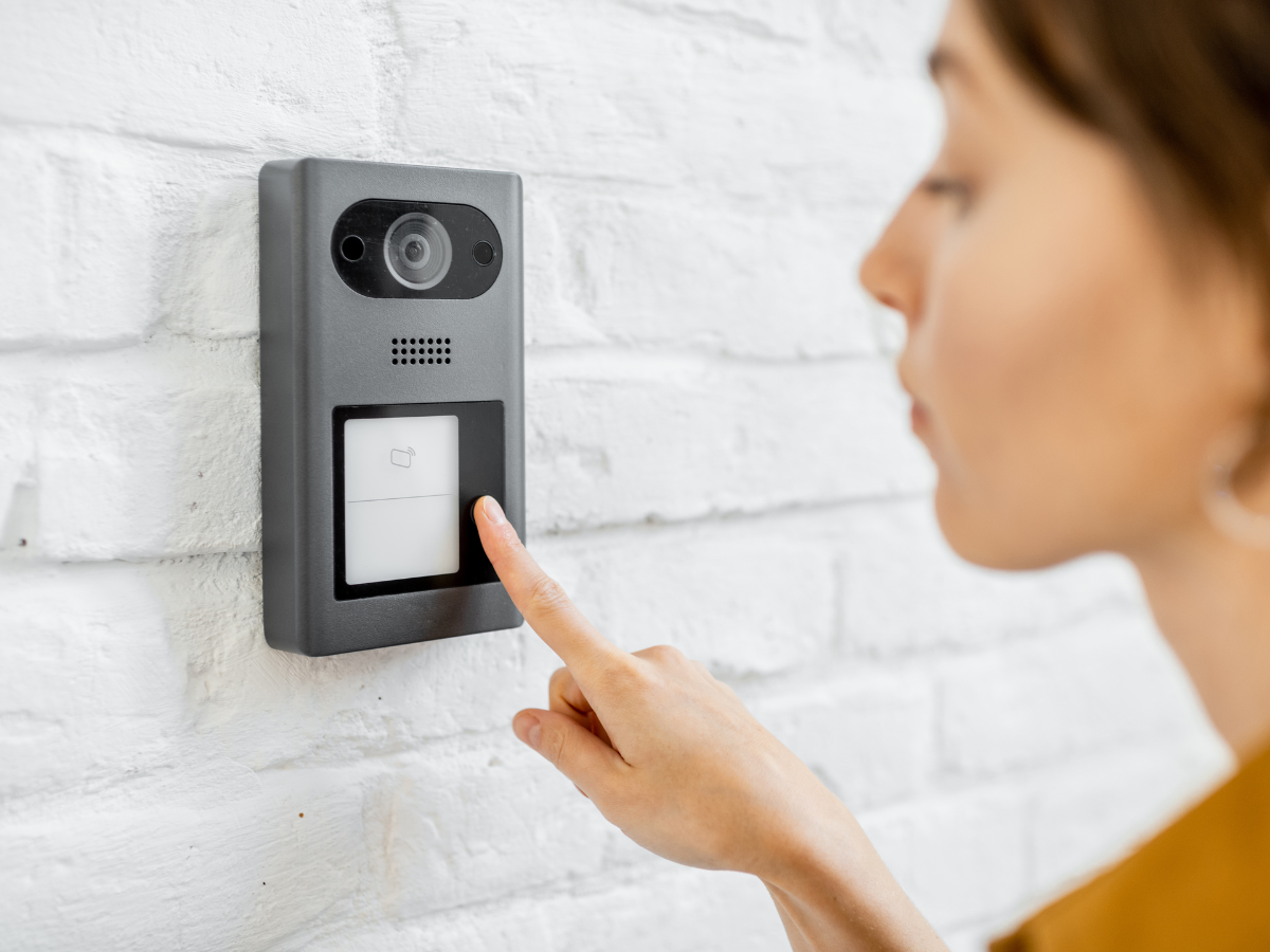 Woman pressing a video cctv doorbell on a white brick wall