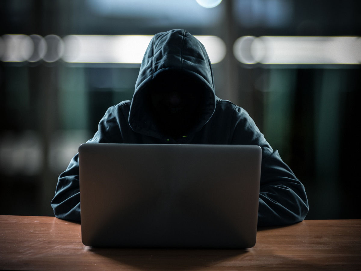 Person wearing a hooded jacket using a laptop in a dimly lit room