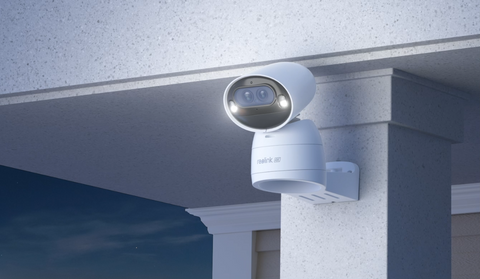 Reolink Argus Track 4K Dual-Lens Wi-Fi Solar/Battery Camera with Auto-Zoom Tracking on front porch at night emitting white spotlight