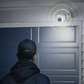 Person wearing a cap looking at a Reolink Altas security camera with lights on a wall.