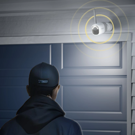 Person wearing a cap looking at a Reolink Altas security camera with lights on a wall.