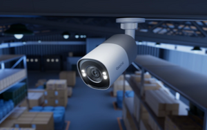 bullet style Security camera with white spotlight in a dark warehouse setting 