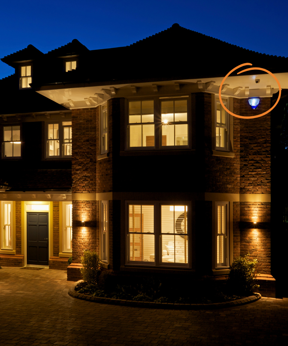 Luxurious house exterior at night with illuminated windows and a security camera highlighted.