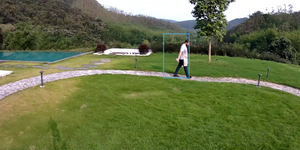 Person walking along a path in a  grassy area with a pool and trees in the background. a blue box highlights the person